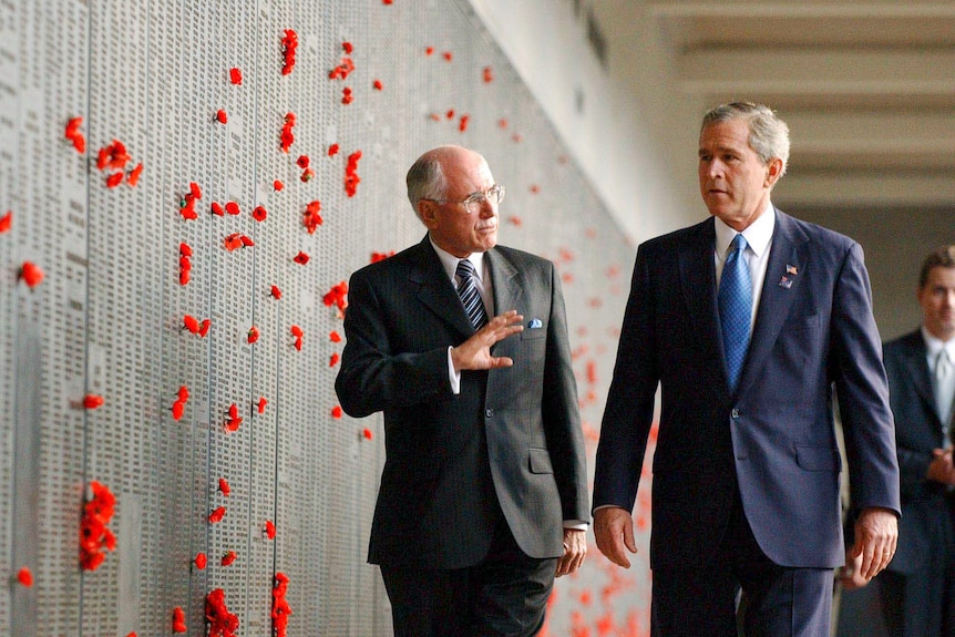 Bush and Howard walk beside a memorial wall marked with poppy flowers.