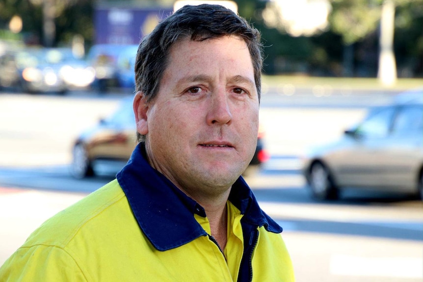 A close up of Jarron wearing a hi-vis shirt with traffic behind him.