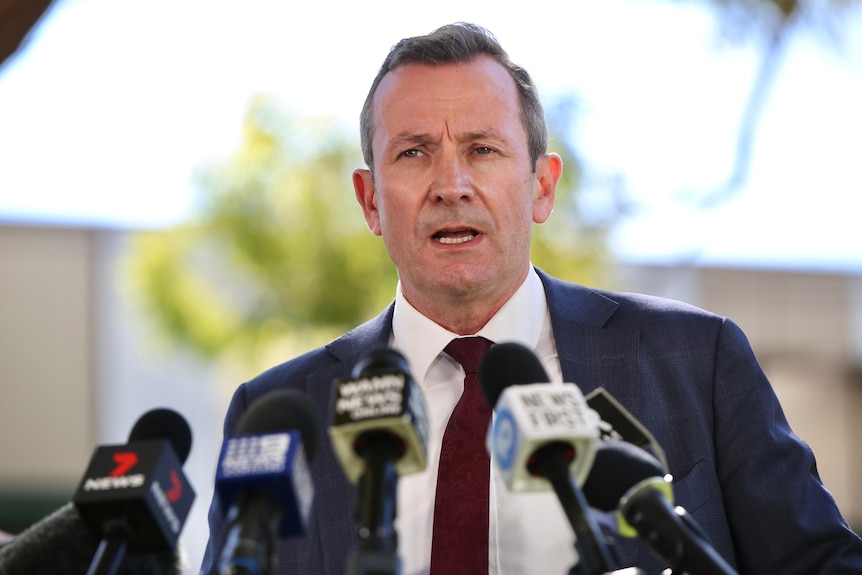 A head and shoulders shot of Mark McGowan talking in front of microphones during a media conference.