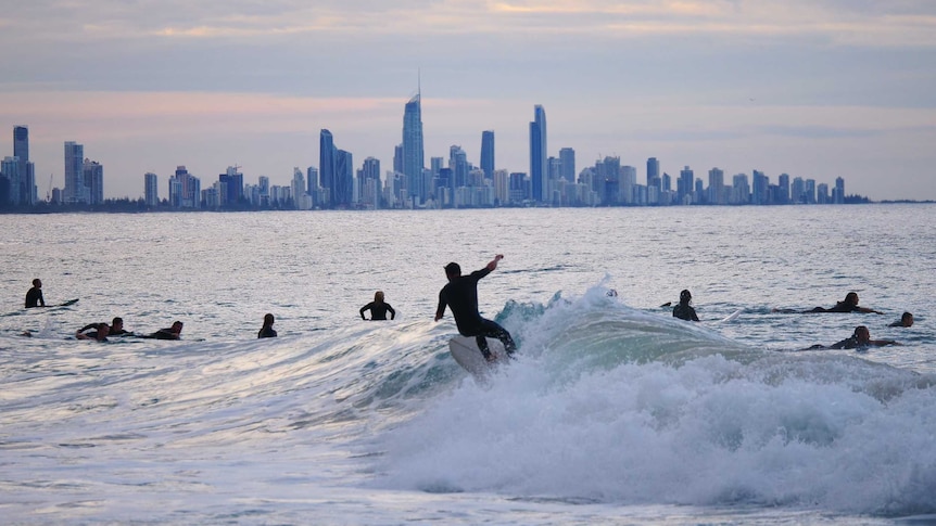 Surfer riding a wave with the Gold Coast's high-rise skyline in the background.