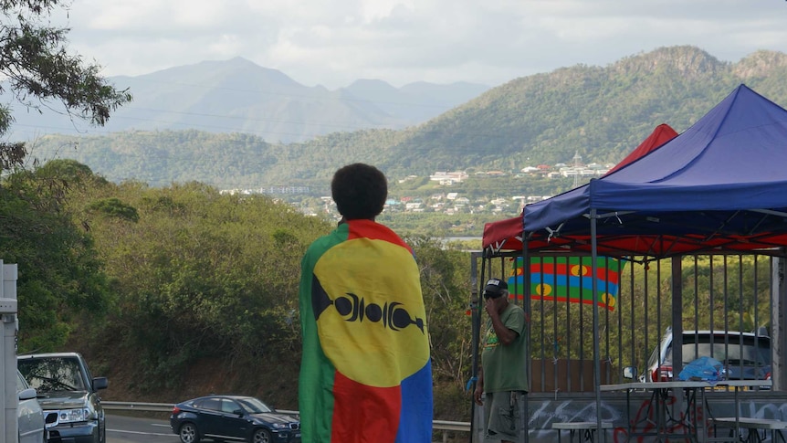 Man draped in Kanaky Flag overlooking hills in New Caledonia