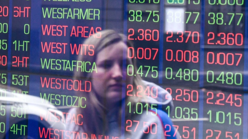 A woman is seen in the reflection of a window while she looks at stock prices on a board of the ASX