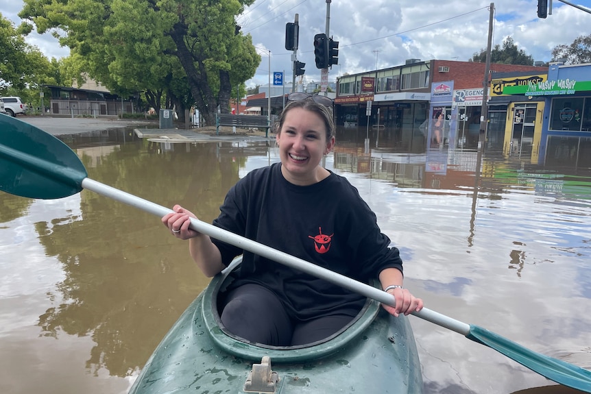 A woman in a kayak paddling through a flooded town.