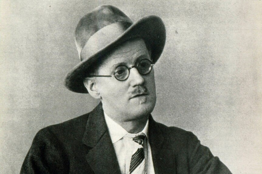 A black and white image of a man wearing a hat, glasses and a suit and tie.