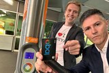 Two men stand with an Opal card in a train station