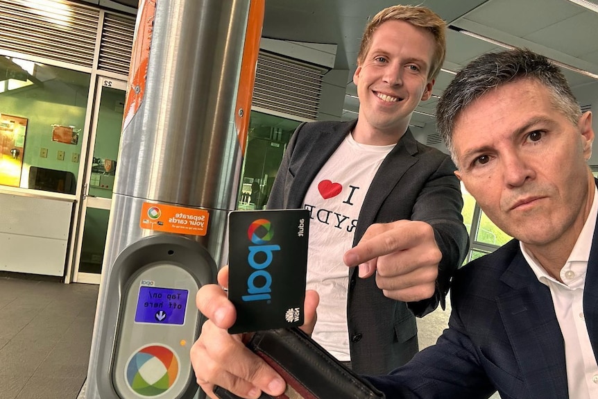Two men stand with an Opal card in a train station
