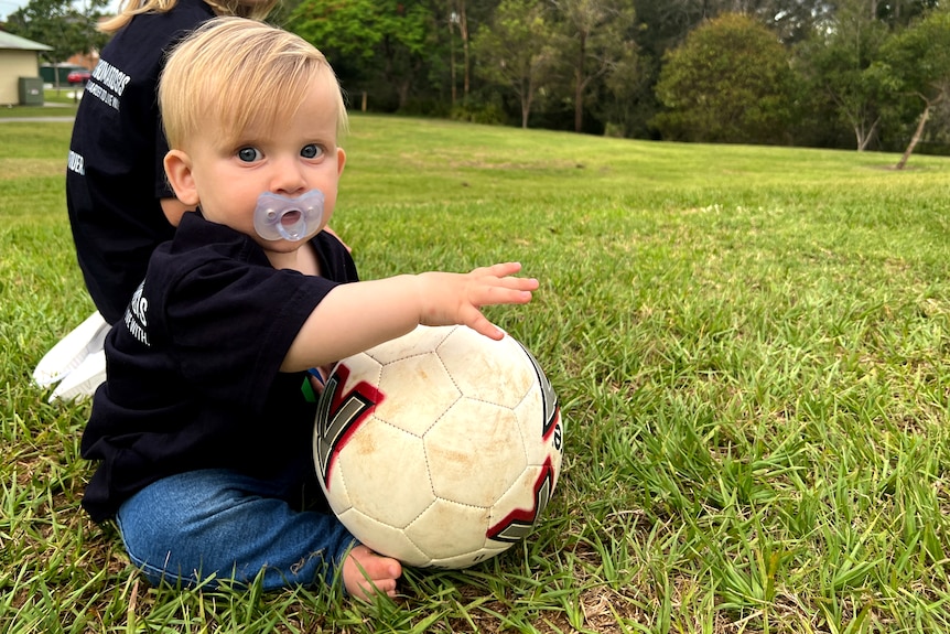 Baby sits on the grass holding a soccer ball