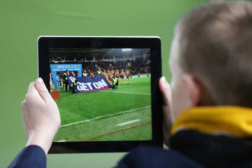 Fan poses with a tablet as teams line up before a match