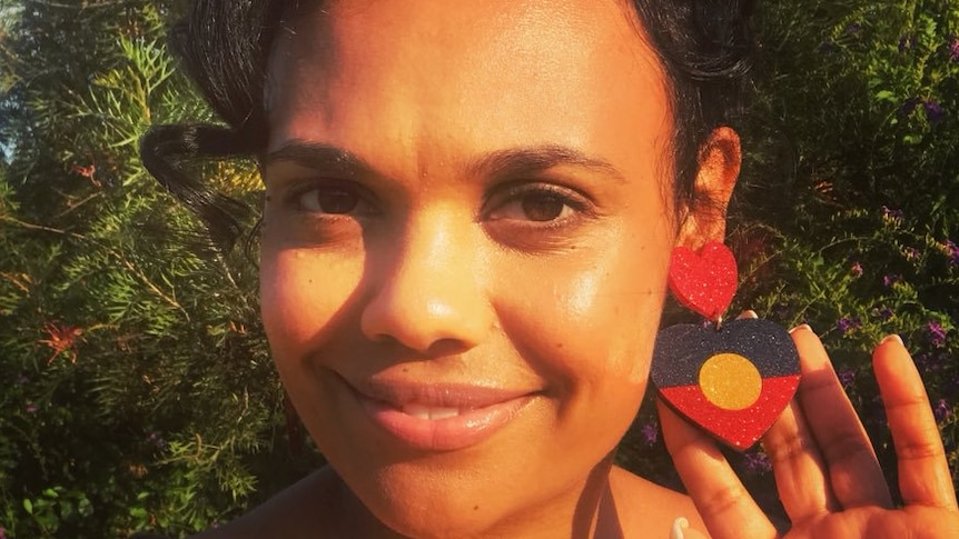 A woman wearing earrings with the Aboriginal flag on them smiling at the camera