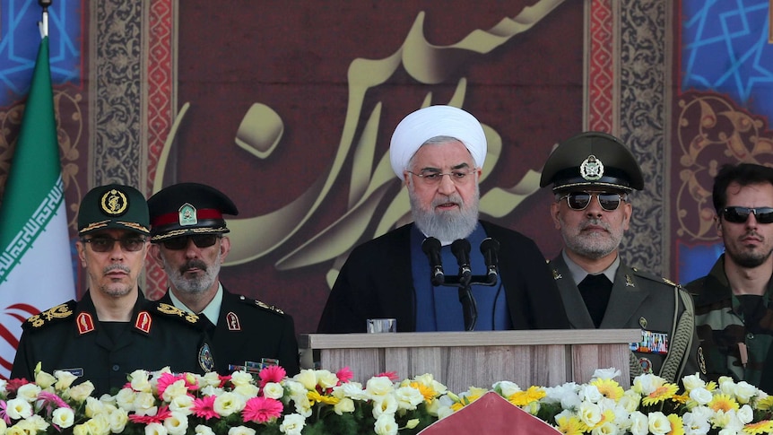 Iranian President Hassan Rouhani flanked by military officials giving a speech.