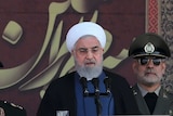 Iranian President Hassan Rouhani flanked by military officials giving a speech.