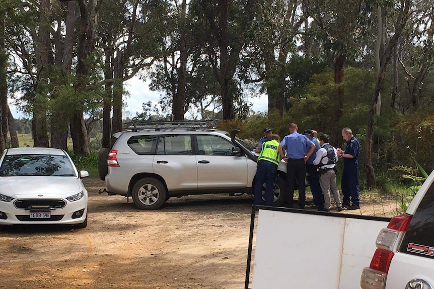 Police officers cluster around a car bonnet, in a bushland area.