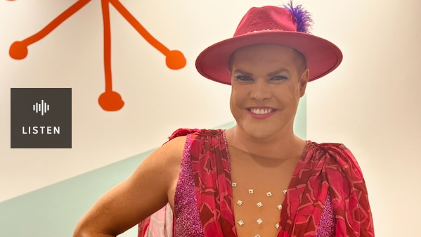 man in pink fedora with purple feather and pink sequinned-sleeveless top smiling . Has Audio
