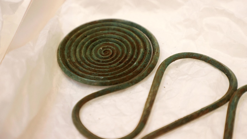 A green-tinged bronze piece of jewellery with a circular swirl. 