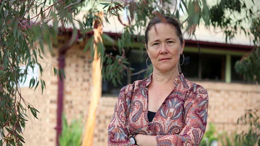 Illawarra Women's Health Centre general manager Sally Stevens stands with her hands crossed under a leafy green tree