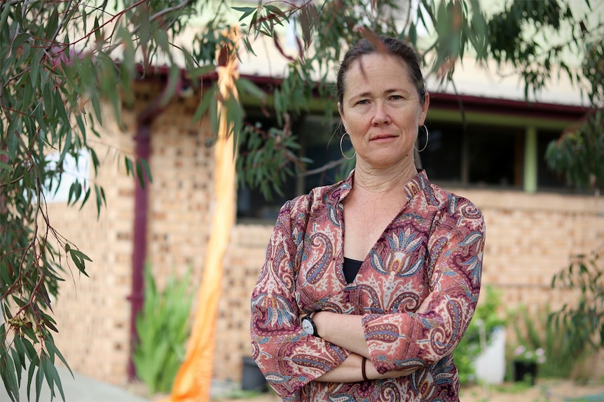 Illawarra Women's Health Centre general manager Sally Stevens stands with her hands crossed under a leafy green tree