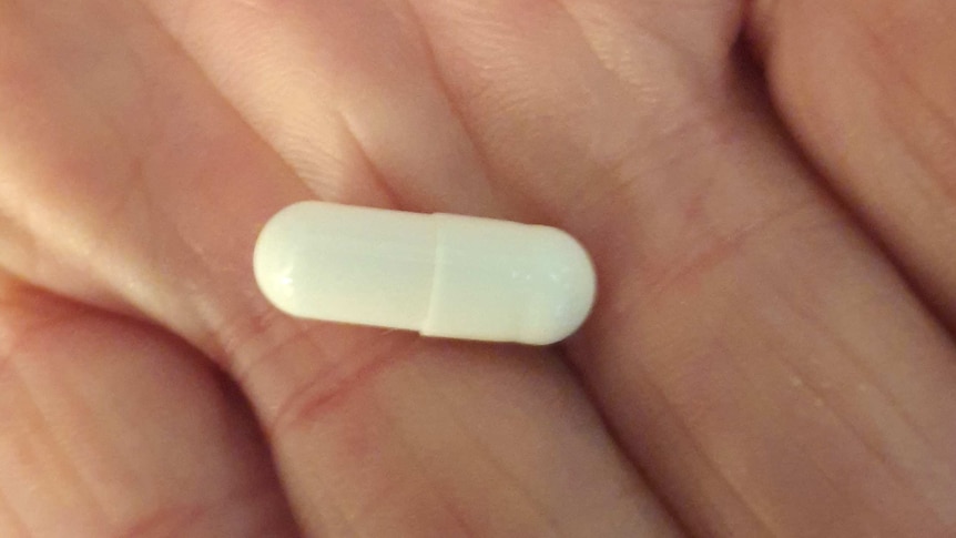 A close-up photo of a white capsule pill on a palm