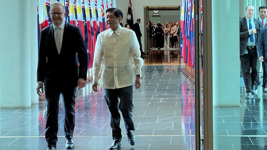 Anthony Albanese walks past flags with Philippine President Ferdinand Marcos Jr at Parliament House as a crowd watches.