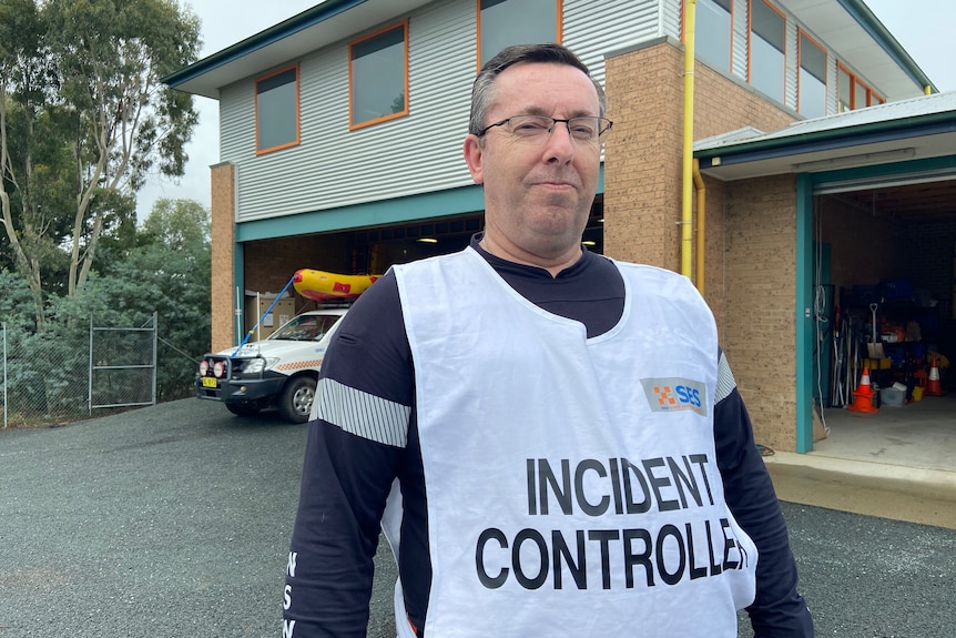 A man wearing an 'incident controller' vest stands in front of an emergency services station