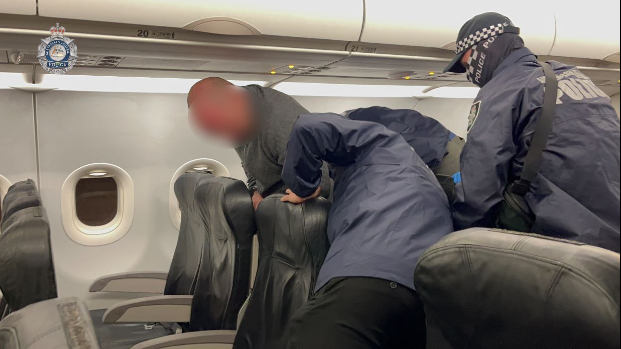 A digitally blurred image of a man being put onto a plane seat by AFP officers.