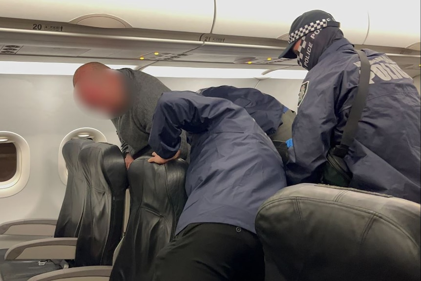 A digitally blurred image of a man being put onto a plane seat by AFP officers.