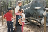 Several people stand looking at a large dinosaur. 