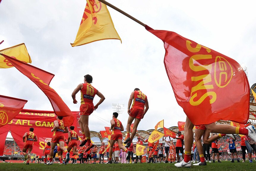 Players run out onto the field as red and gold Suns flags fly.