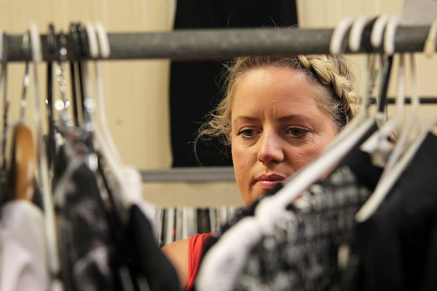 A photo of Kelly Wright as she sorts through a garment rack in front of the camera.