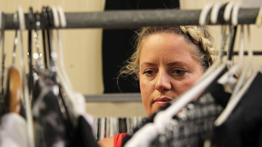 A photo of Kelly Wright as she sorts through a garment rack in front of the camera.