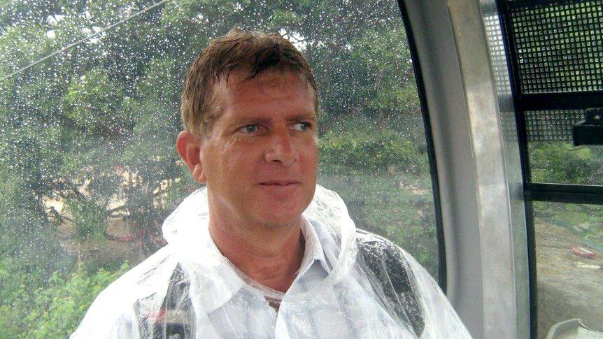 A man riding on a cable car in the rain, wearing a see-through plastic poncho.