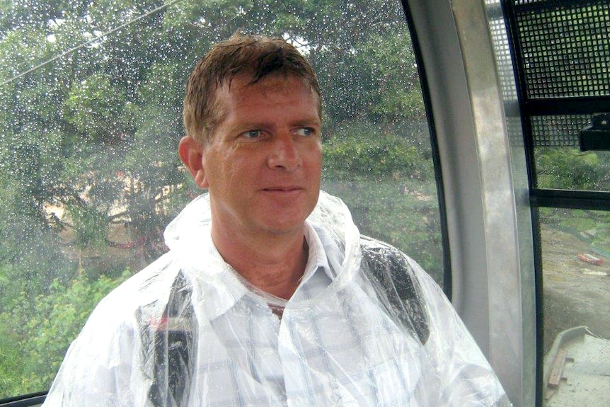 A man riding on a cable car in the rain, wearing a see-through plastic poncho.