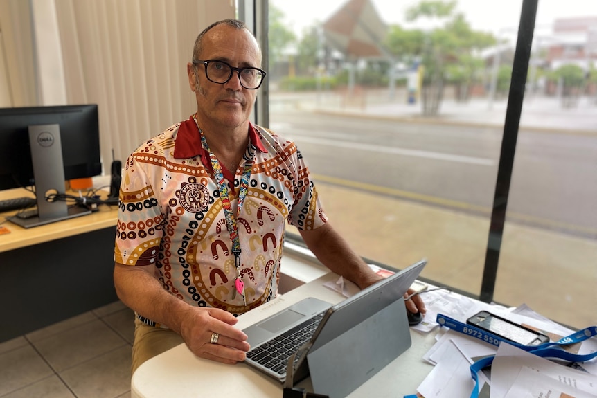 a man wearing glasses and a shirt with an indigenous print working on a laptop