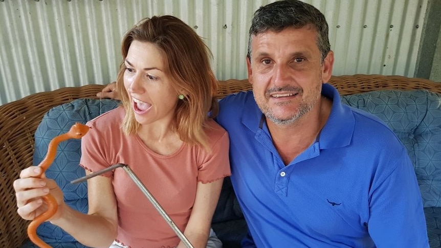 A woman holding a toy snake makes a face of mock alarm while her husband smiles for the camera.