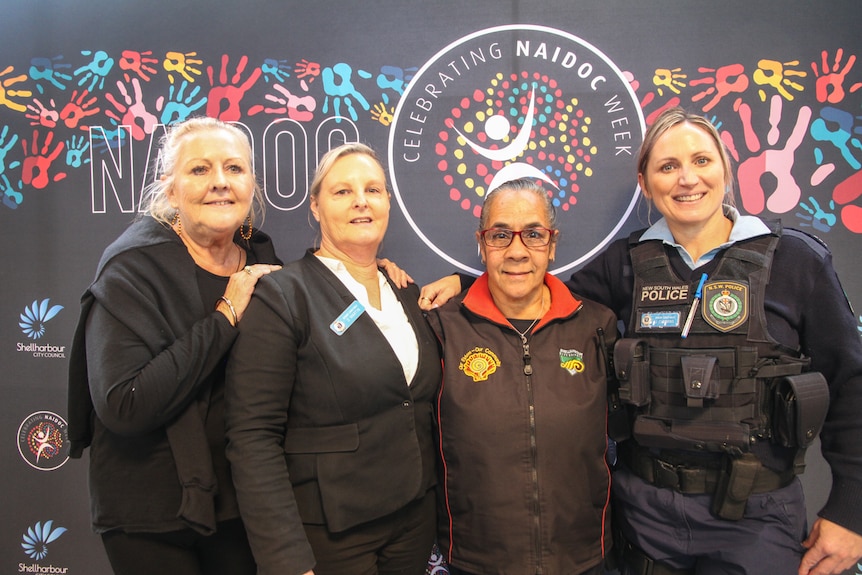 Four women smile in front of a colourful wall