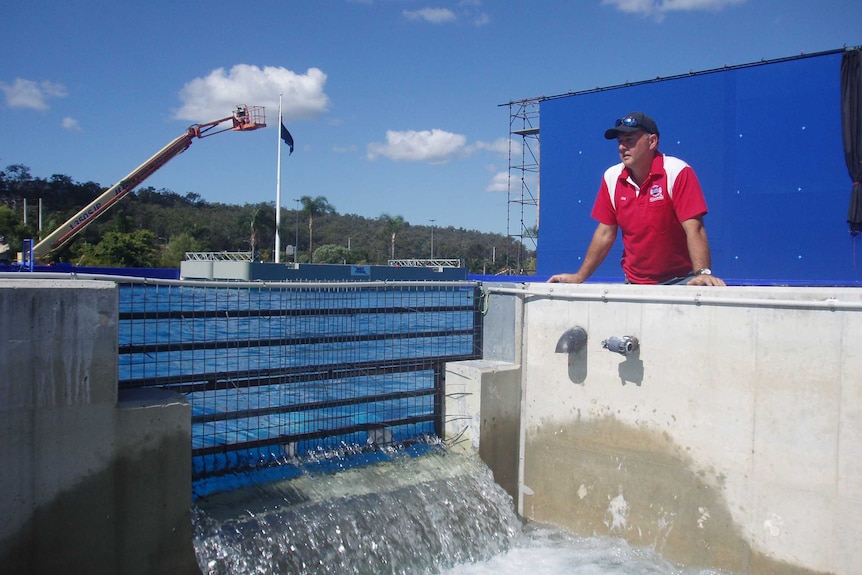 a man in a red polo shirt wearing a cap looks the side of giant pool where blue water in flowing through a grate