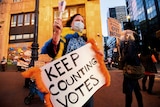A woman holding a sign that says 'keep counting votes'