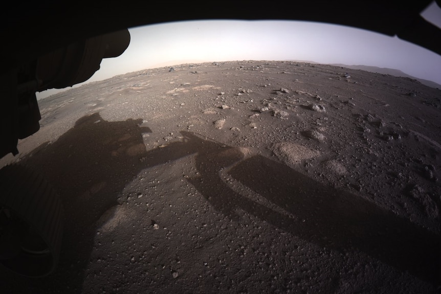 An aerial view of a rocky and desolate planet with the shadow of a low-flying space craft.