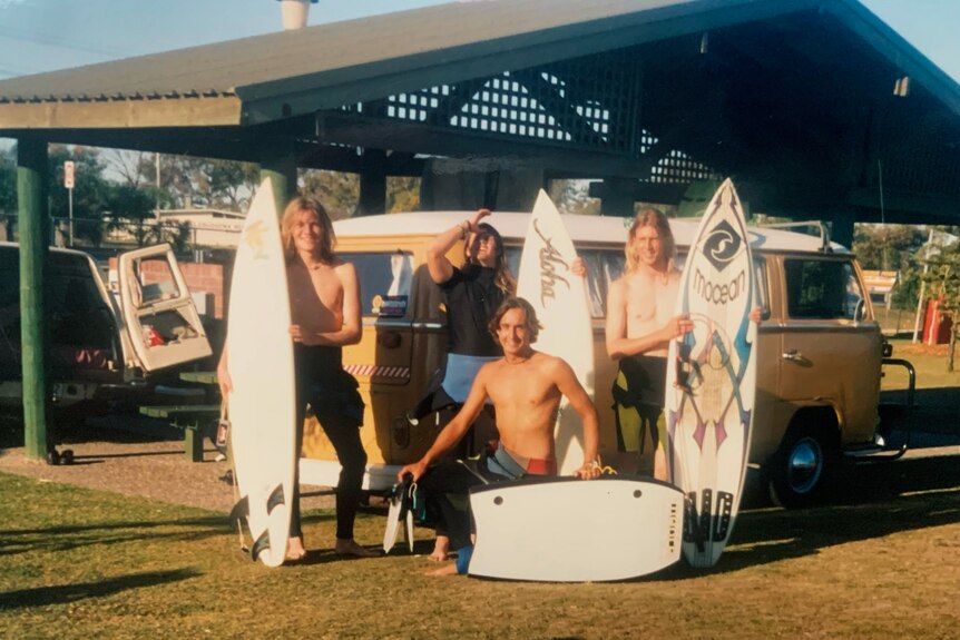 An old photo of four teenage boys standing with surfboards, smiling.
