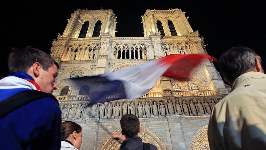 A man waves a France flag on the square outside Paris' Notre Dame Cathedral.