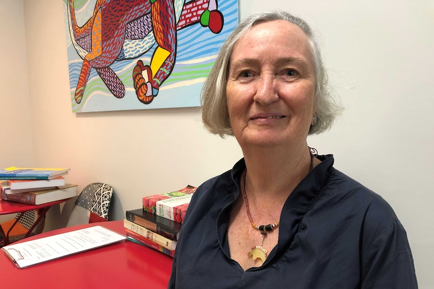 A woman in an office with an Indigenous painting on the wall and academic books scattered across two tables