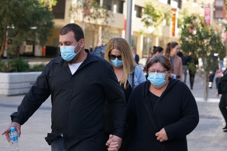 Three people in face masks walk along a city street. 
