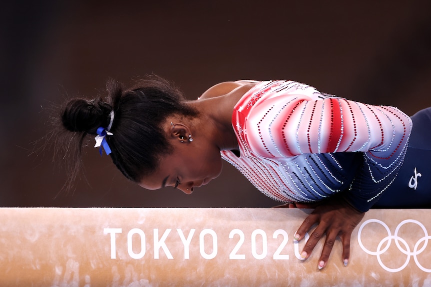 Simone Biles looks down at the beam while balancing on it. She is wearing her US team leotard