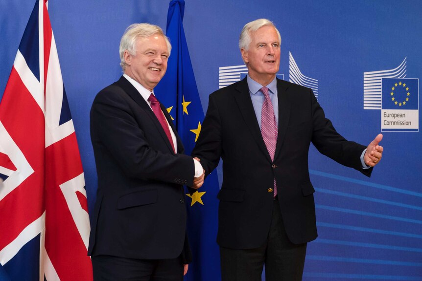 Michel Barnier and David Davis shake hands in front of British and EU flags.