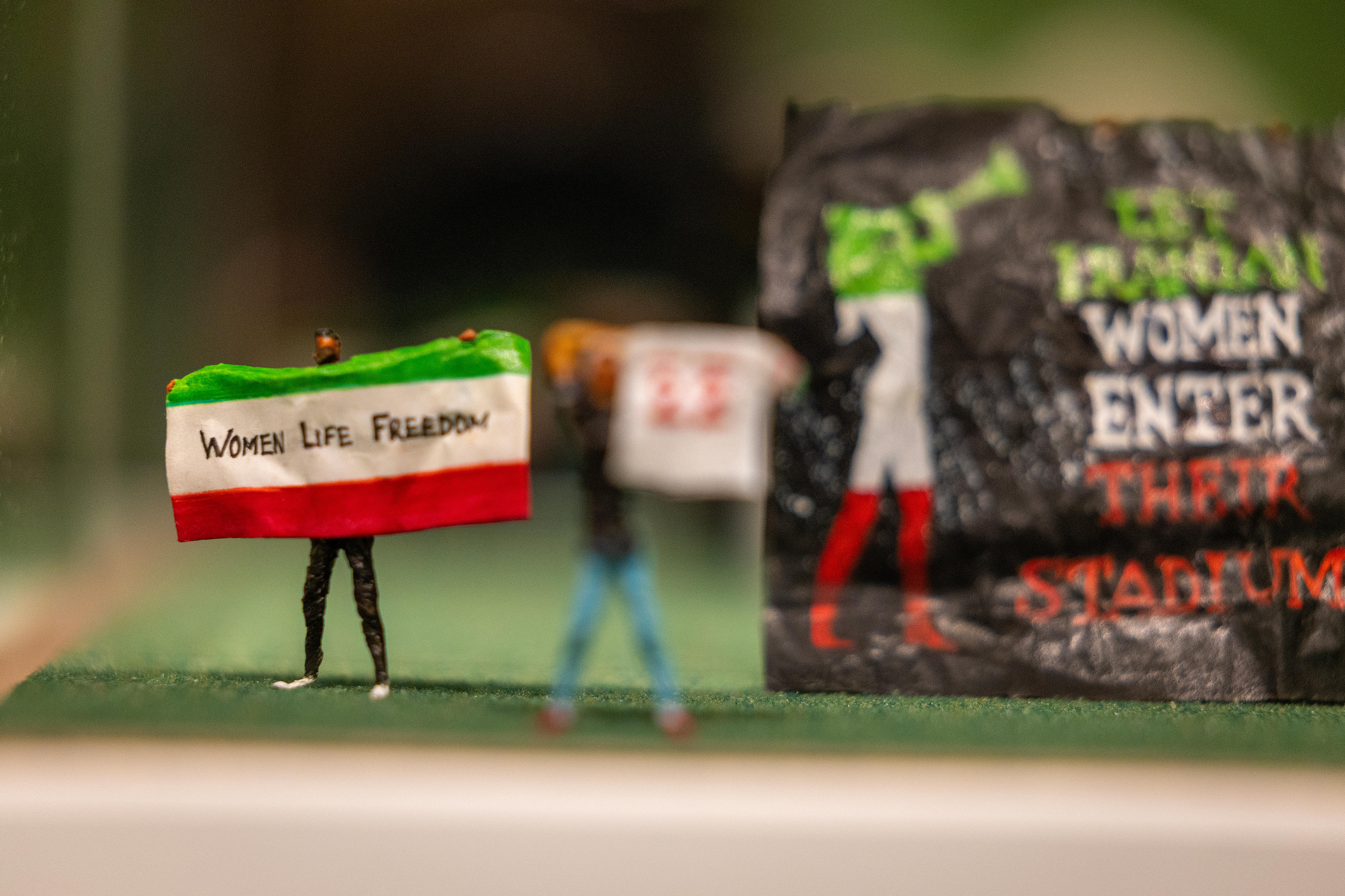 A miniature figurine of a person holding an Iranian flag with the words 'women, life, freedom'