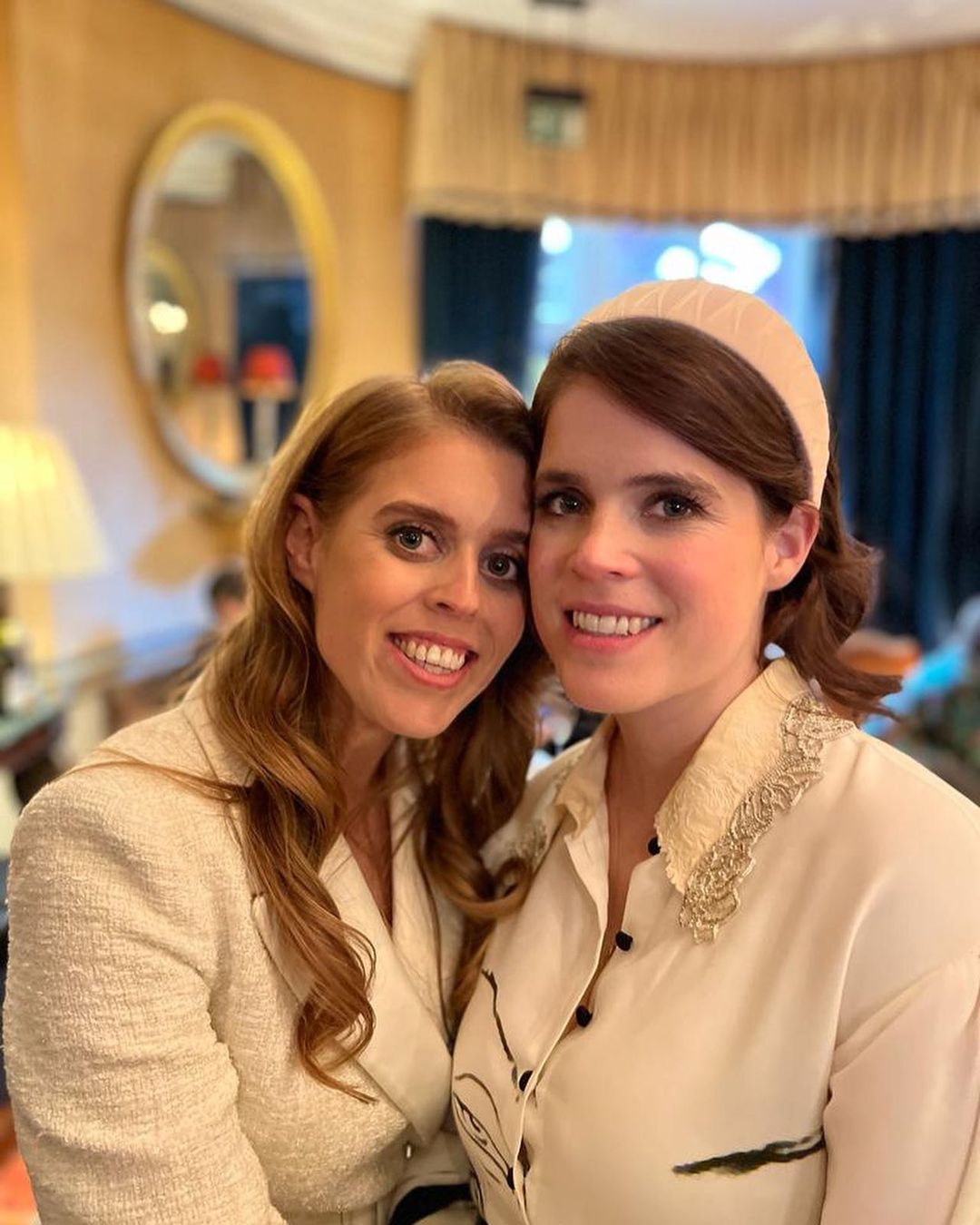 A close up of Princess Beatrice and Eugenie dressed in white jackets hugging each other and smiling.