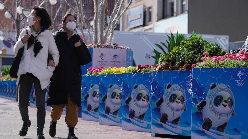 Women wearing face masks walk past images of the Beijing Olympic mascot, a panda
