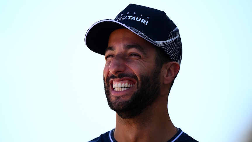 Daniel Ricciardo smiles widely while wearing an AlphaTauri hat