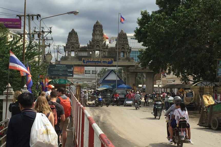 People walk and drive towards the Cambodia-Thailand border crossing.