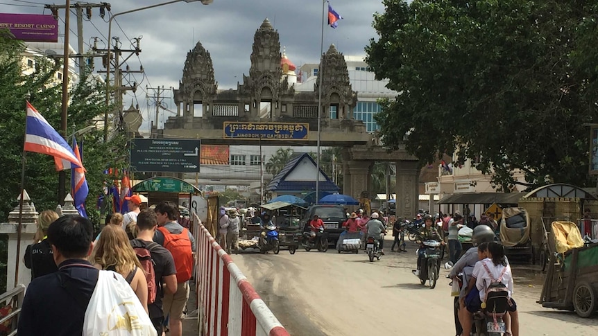 People walk and drive towards the Cambodia-Thailand border crossing.
