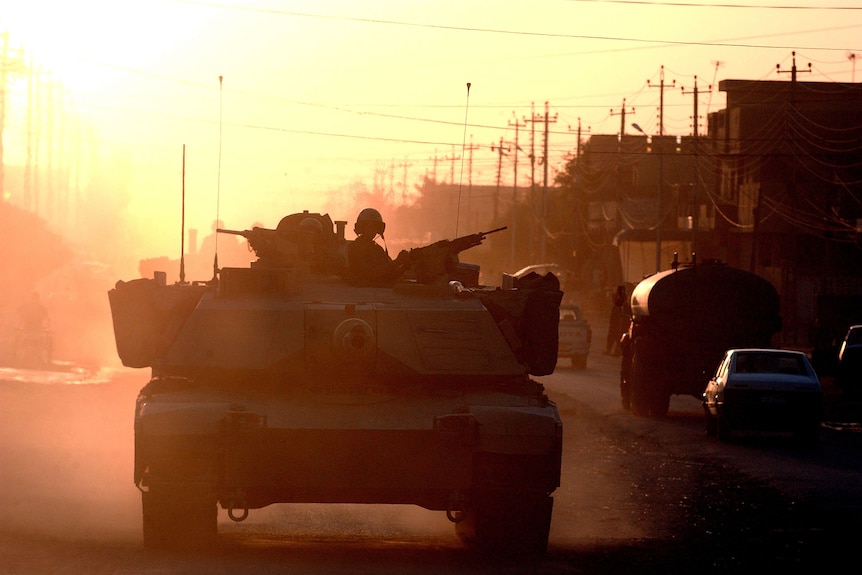 Silhouette of army tank and soldier manning machine gun. Sun is low in the background producing golden-orange light